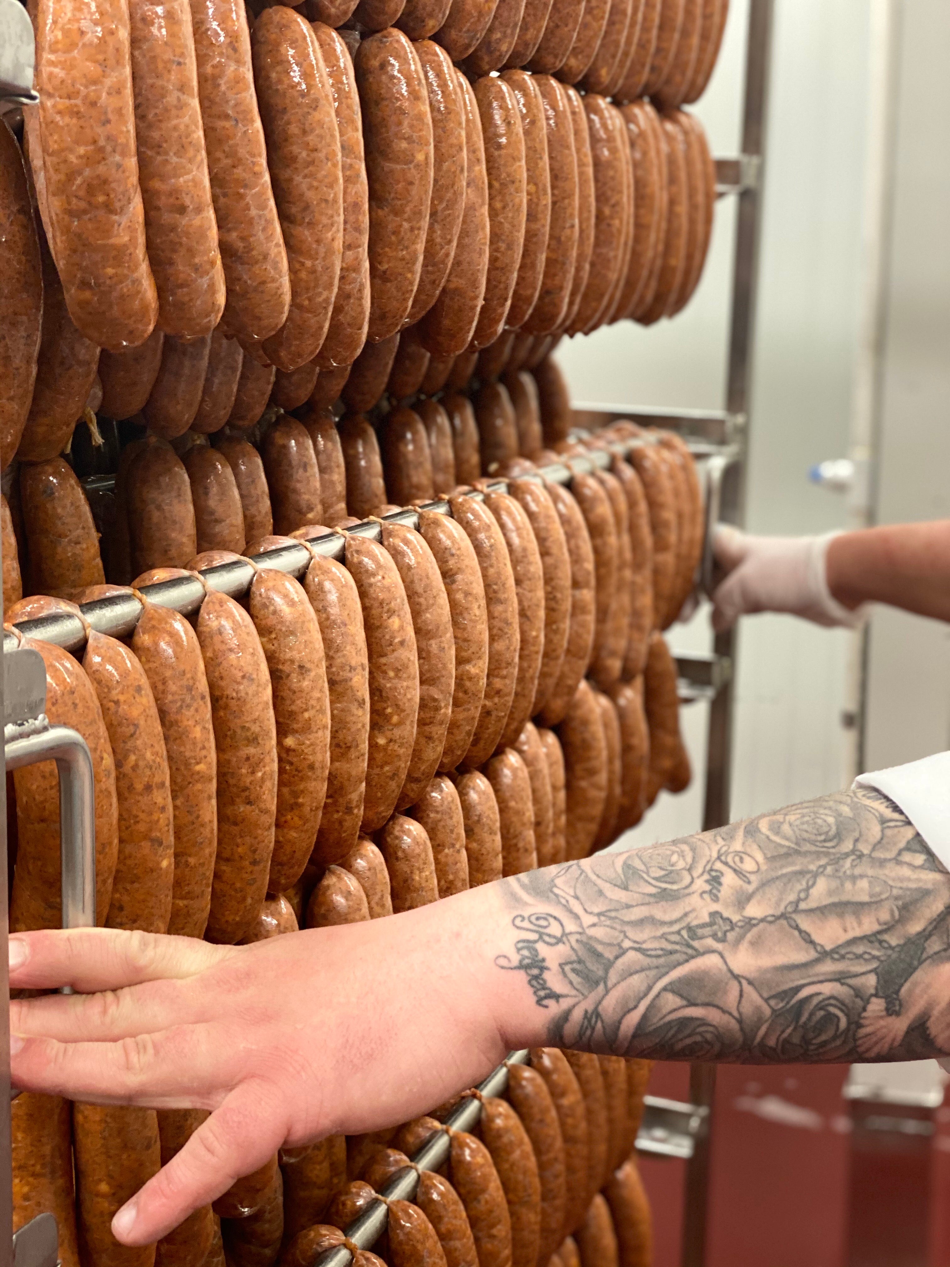 Hands guiding a rack filled with andouille sausage links