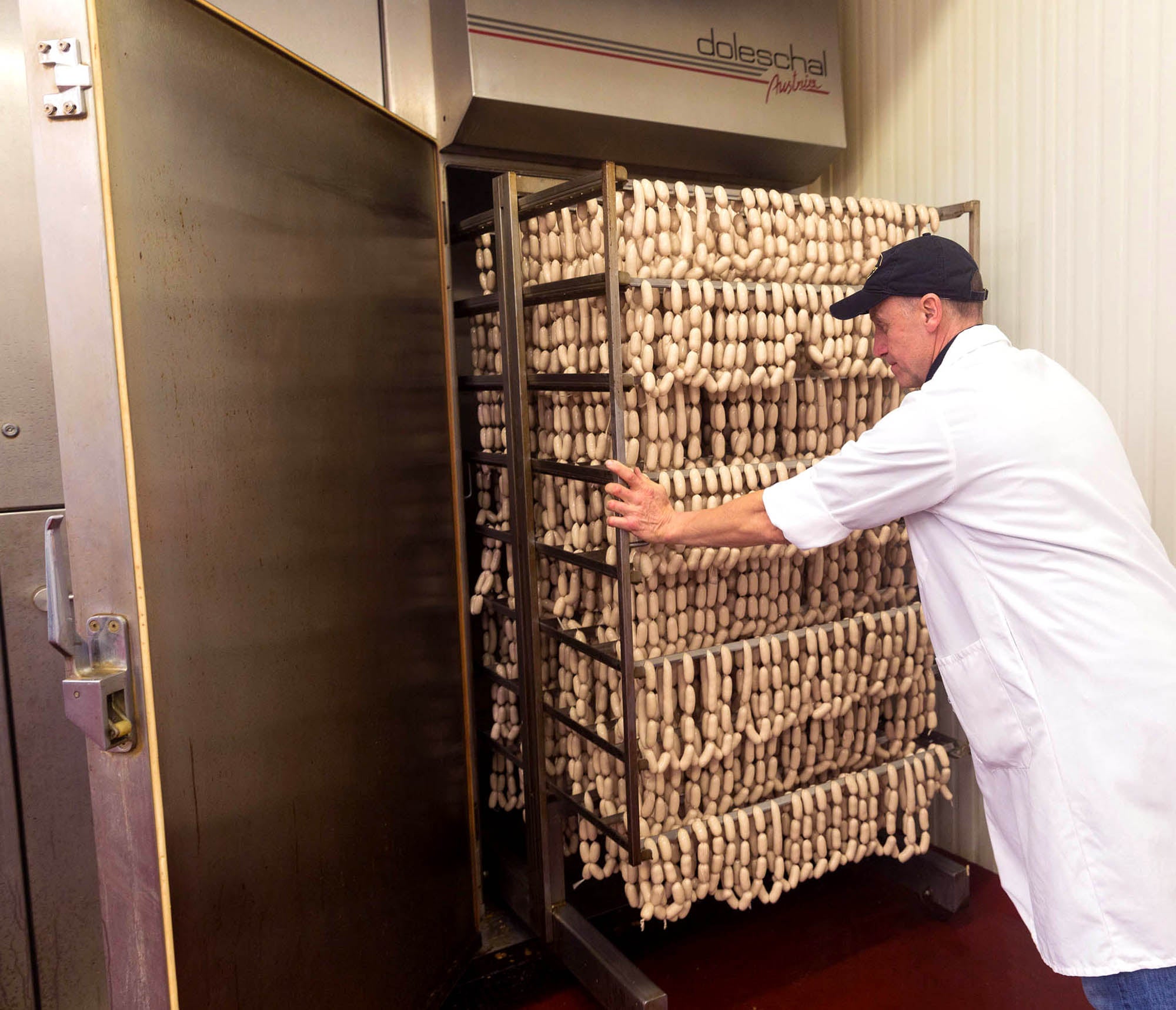 Josef’s artisan in a production room beside racks of hanging sausages.